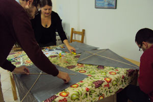 Bild: drei Eltern montieren auf einem Tisch je einen Drachen