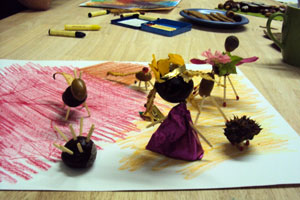 Bild: Kastanienmännchen und -tiere auf einem bunt bemalten Blatt Papier auf einem Tisch