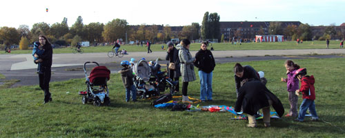 Bild: Erwachsene und Kinder beim Drachen zusammenbauen auf einem großem Feld