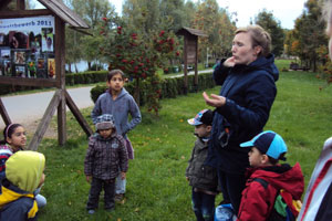 Bild: Mutter erklärt auf eine Wiese stehend einigen um sich gescharten Kindern etwas
