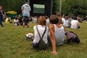 Bild: Menschen sitzen mit dem Rücken zum Betrachter auf eine Wiese und schauen auf die Leinwand im Hintergrund
