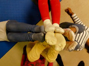 Foto: vier in kreuzform auf dem Rücken liegende Kinder strecken ihre Füße noch oben, in Richtung Betrachter und berühren sich alle an ihren Fußsohlen.